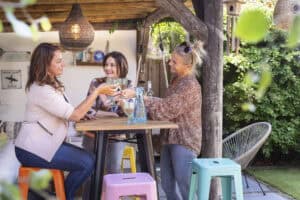 Vriendinnen genieten van een drankje in de tuin onder een houten overkapping.